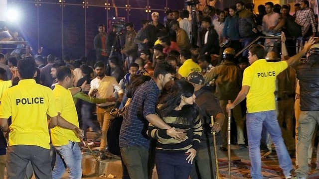 An Indian man helps a woman leave as police personnel try to manage crowds during New Year’s Eve celebrations 2016 in Bengaluru. (STR/AFP/Getty Images)