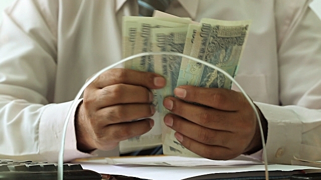 A bank teller counts notes. (GettyImages)