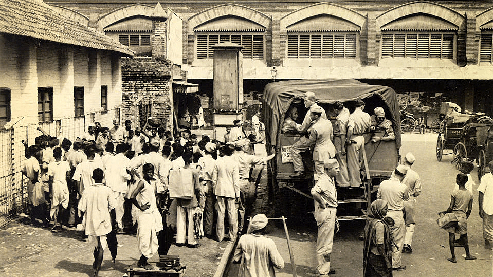 

Crowd gathers around a sidewalk performer at a bus stop while GIs take temporary advantage of an overhead view from the steps of a camp bus.