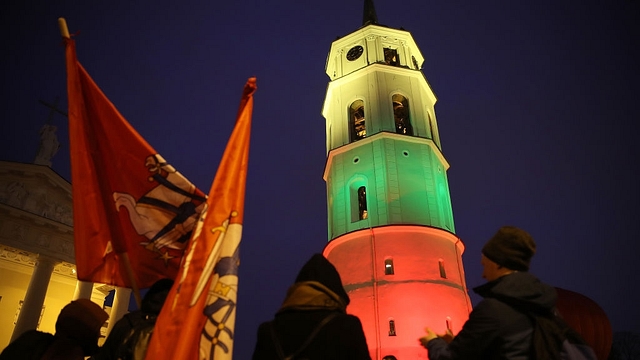 People dance next to the bell tower of Vilnius Cathedral as it stands illuminated in the colours of the Lithuanian flag to mark the 100th anniversary of the restoration of Lithuanian statehood in Vilnius, Lithuania. (Sean Gallup/Getty Images)