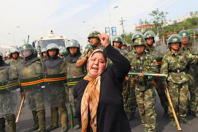 A protesting Uyghur woman surrounded by Chinese security personnel. (pic via Twitter)