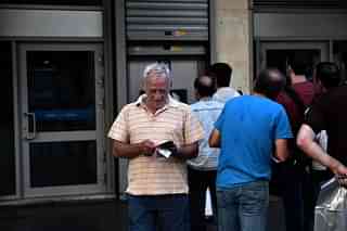 People queue outside a bank to withdraw cash from an ATMAFP PHOTO / ARIS MESSINIS