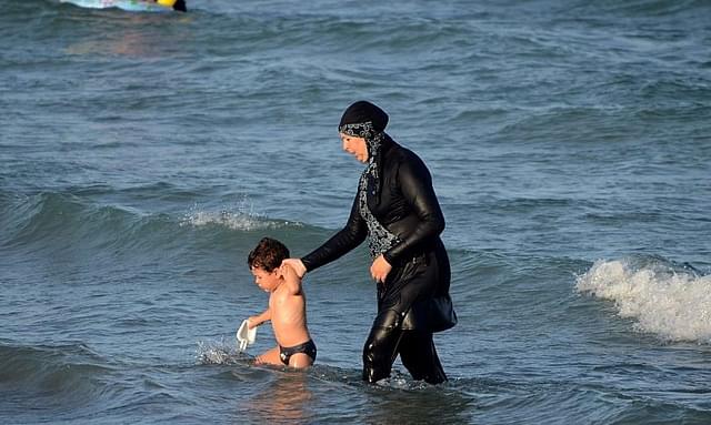 A woman wearing a burkini walks in the water with a child. Photo
credit: FETHI BELAID/AFP/GettyImages &nbsp; &nbsp; &nbsp;