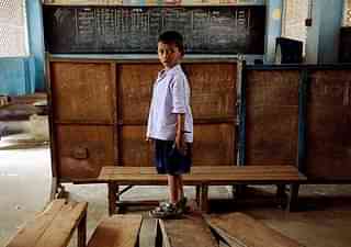 A schoolboy stands on a bench in an empty classroom