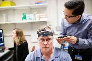 

Research fellow Ali Jannati simulates a TMS therapy session on John Elder Robison as he sits in the room where he took part in brain therapy known as TSM (Transcranial magnetic stimulation) at Beth Israel Hospital in Boston, Mass. (Keith Bedford/The Boston Globe via Getty Images)