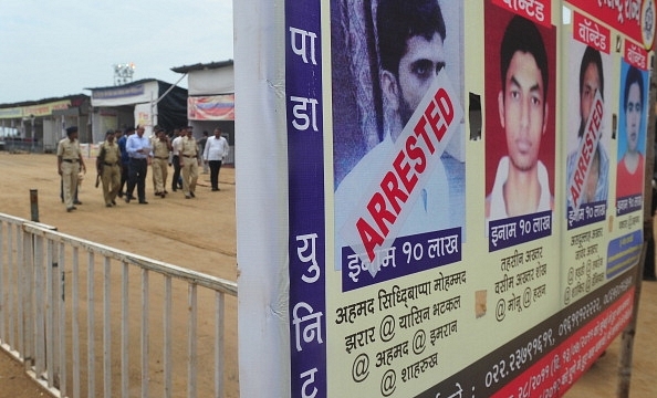 A police team walk past a poster featuring Yasin Bhatkal. (INDRANIL MUKHERJEE/AFP/GettyImages)&nbsp;