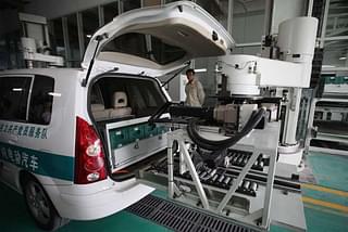 A Chinese worker looks on as a robot changes an electric car’s batteries. (Feng Li via GettyImages) 