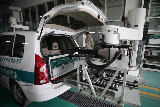 A Chinese worker looks on as a robot changes an electric car’s batteries. (Feng Li via Getty Images)&nbsp;