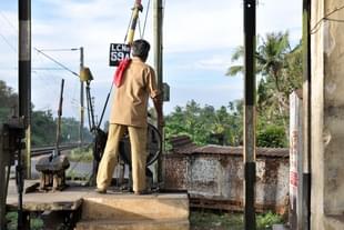 A railway gatekeeper closes the gate at a level crossing. (Image- Joe Ravi via Wikimedia Commons)