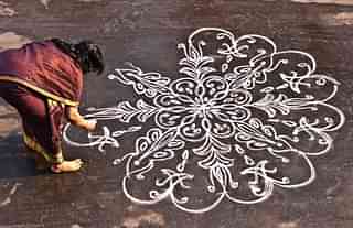A woman works on a <i>kolam</i> in front of her house.