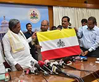 Former Chief Minister Siddaramaiah unveiling the ‘Naada Dwaja’ after a meeting of the flag committee members comprising experts and representatives of pro-Kannada organisations. (Image courtesy of twitter.com/INCKarnataka)&nbsp;