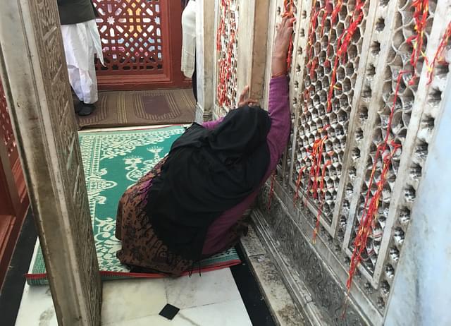 A woman prays from behind the stone-latticed wall on three sides of the main shrine.