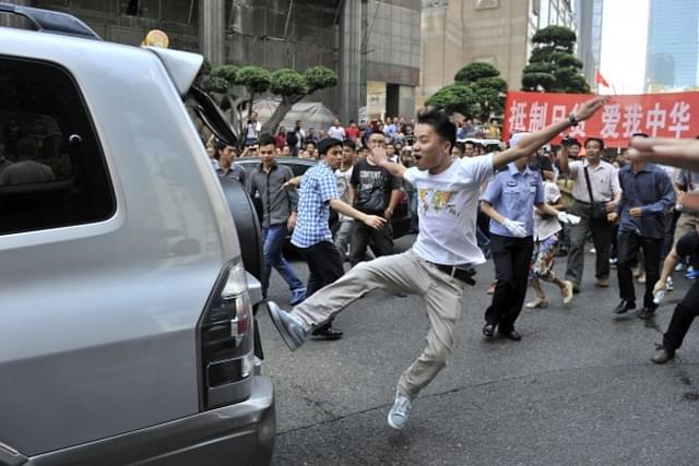 A youth during an anti-Japanese demonstration taking his anger out on a car.