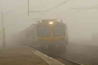 A train at a railway platform, surrounded by thick fog. 