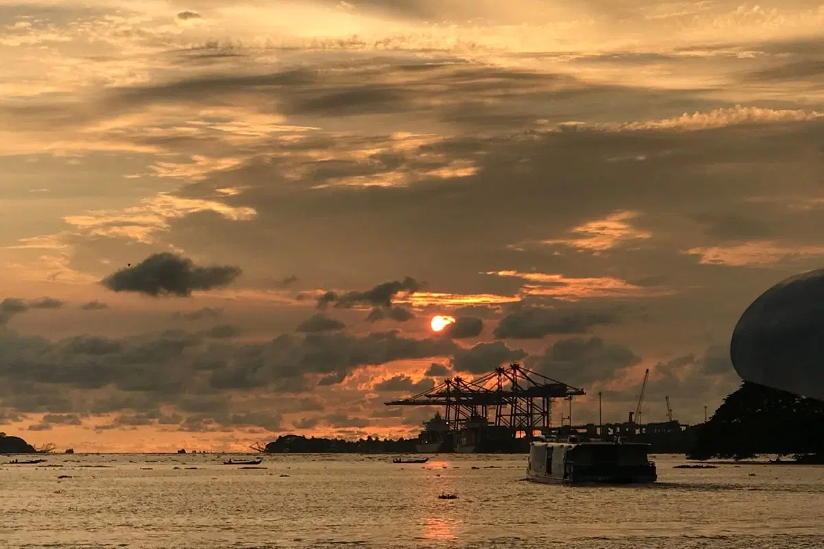 One of the Kochi Water Metro boats passes the towering gantry cranes.
