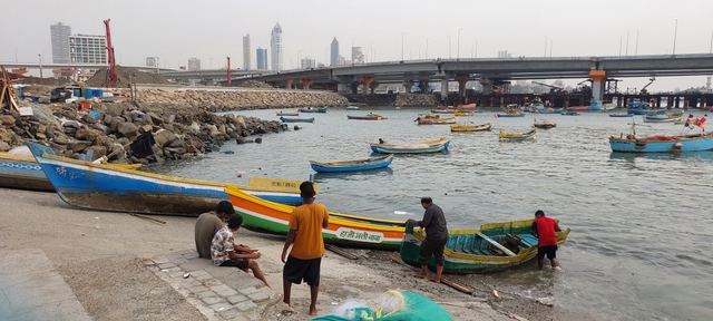 Fishermen pulling boats back to the shore at the Lotus Jetty near Worli. An under-construction segment of the Coastal Road Project in the background.