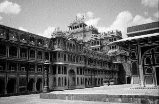 Street front of a Jaipur haveli with shops below and continuous balconies above, creating one shared facade.